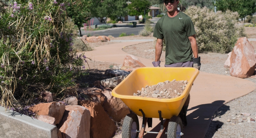 A person pushes a wheelbarrow full of rocks during a service project with outward bound.